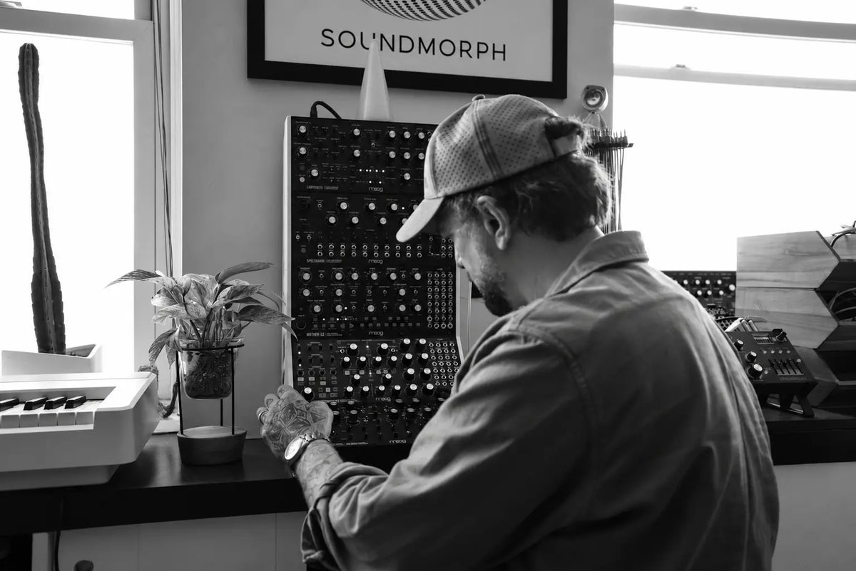 Jason Cushing adjusting a stack of Moog synthesizer modules in the studio, in black and white.