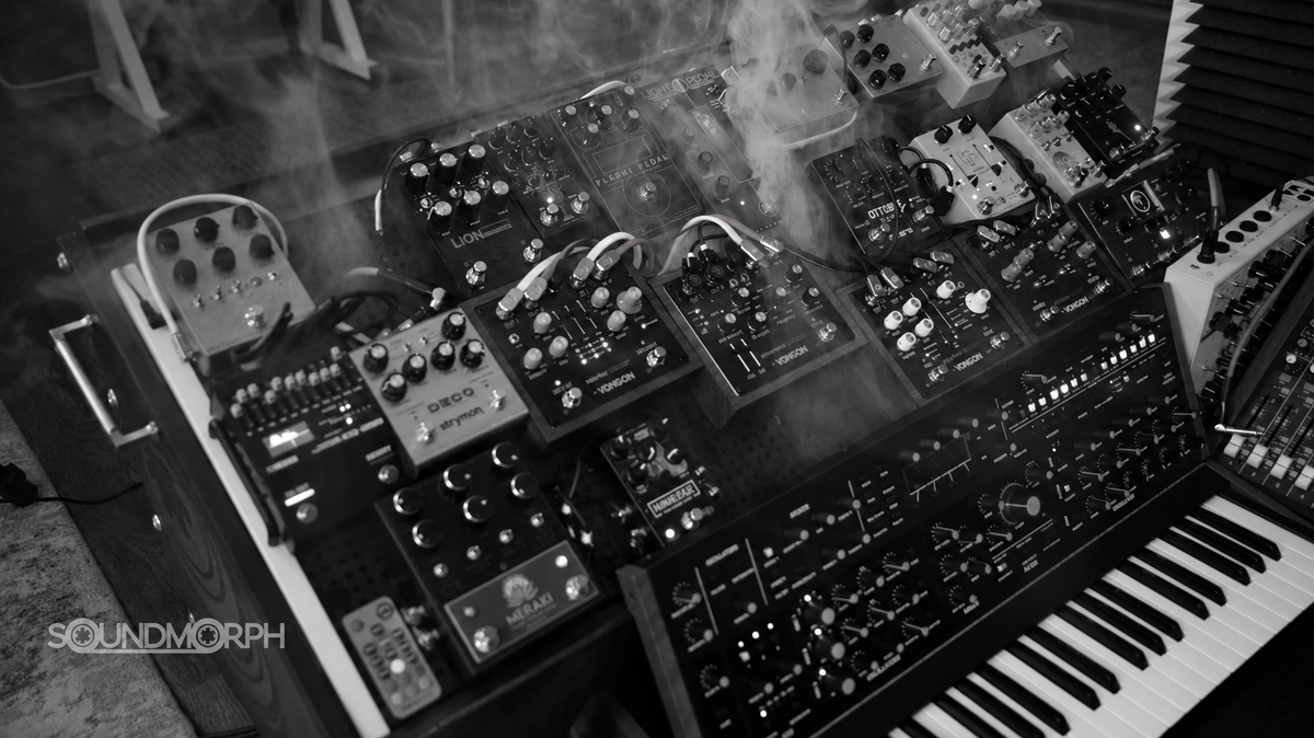 Effects pedals and synthesizers surrounded by studio haze, in black and white.