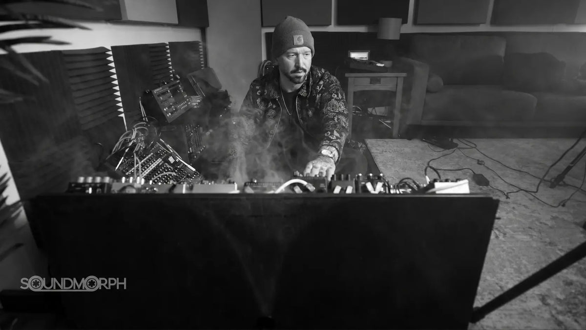 Jason Cushing at the studio console among synthesizers and a light haze, in black and white.